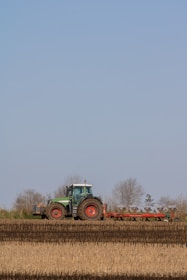A tractor tilling a rich, dark soil field under a clear blue sky.