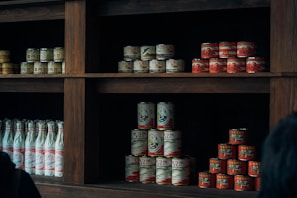 Rows of various canned and bottled food products lined up in a small grocery store aisle