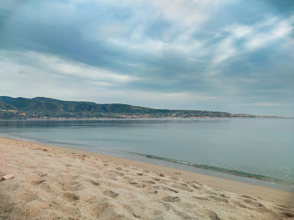 Ein Strand mit einem Gewässer und Hügeln im Hintergrund