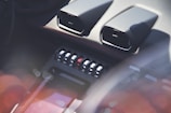 The image displays a luxury car interior featuring air vents, a series of toggle switches, and glossy surfaces. The lighting creates a soft, reflective appearance with hints of lens flare.