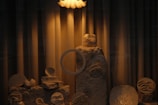 A dimly lit display featuring a variety of abstract sculptures made from natural materials. The scene includes textured stones and uniquely shaped ceramic pieces, arranged artistically on a small platform. The lighting casts warm, soft shadows across the objects, enhancing their textures and forms.