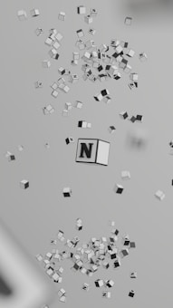 Numerous small cubes with the letter 'N' on them are floating in a three-dimensional space. The cubes are primarily in shades of gray and have a clean, minimalistic design.