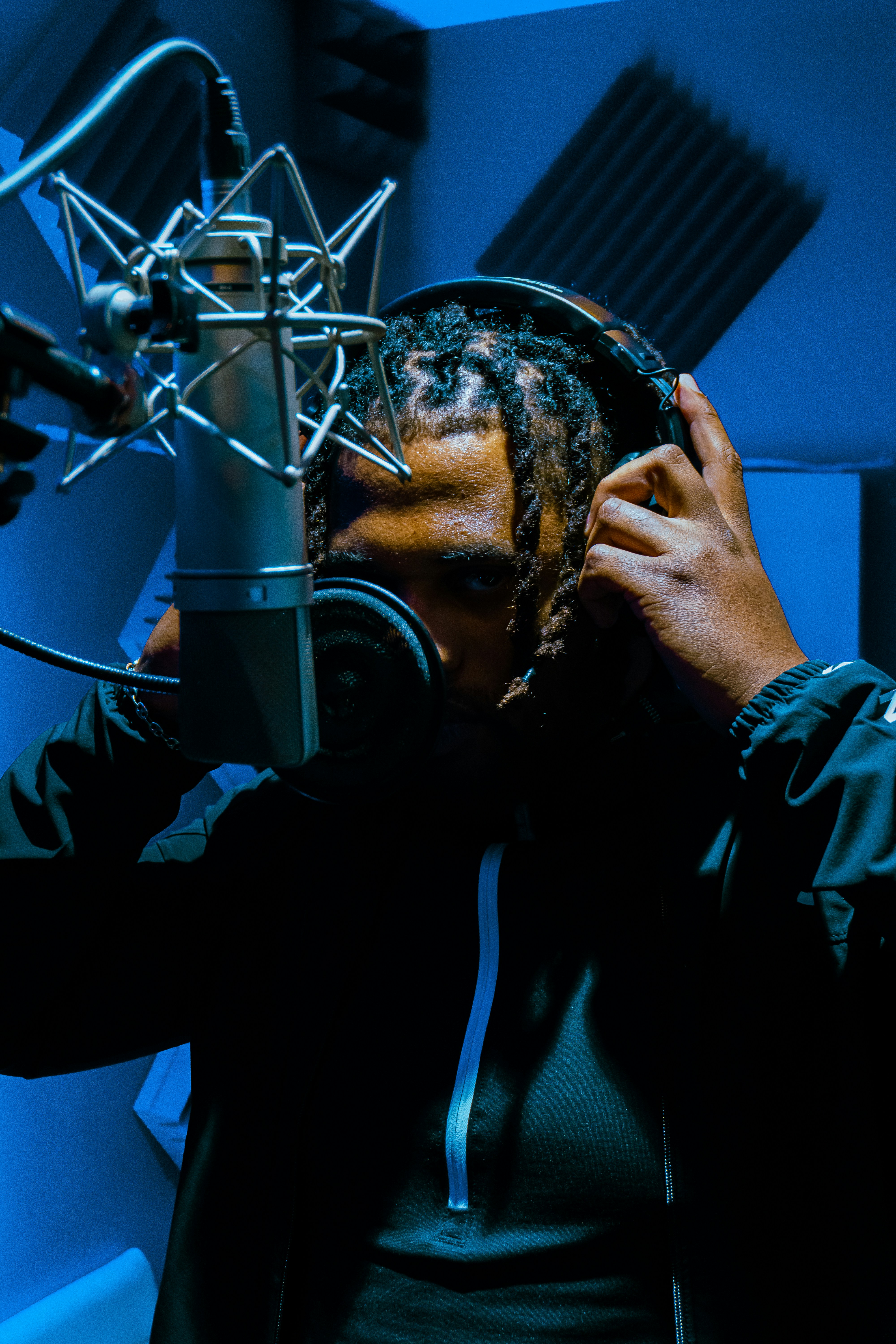 Content creator with dreadlocks in dark moody studio, low-key atmospheric lighting, deep shadows, professional dark background