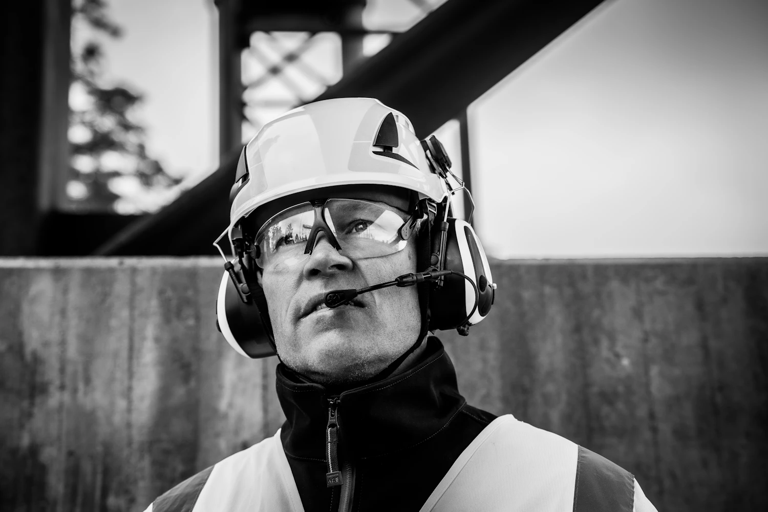 A technician in a helmet with ear defenders and clear goggles, lit from the side