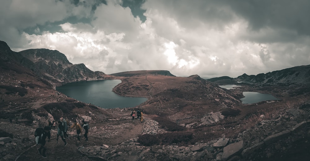 a group of people walking on a rocky path by a body of water