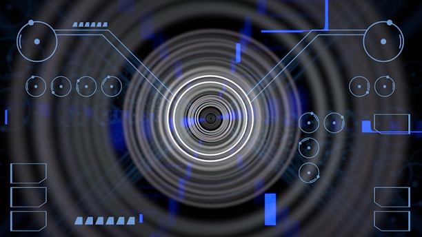 A futuristic digital display featuring geometric shapes, concentric circles, and circuit-like patterns. Various lines and circular elements are spread across a dark background, giving a high-tech appearance.
