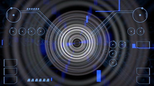 A futuristic digital display featuring geometric shapes, concentric circles, and circuit-like patterns. Various lines and circular elements are spread across a dark background, giving a high-tech appearance.