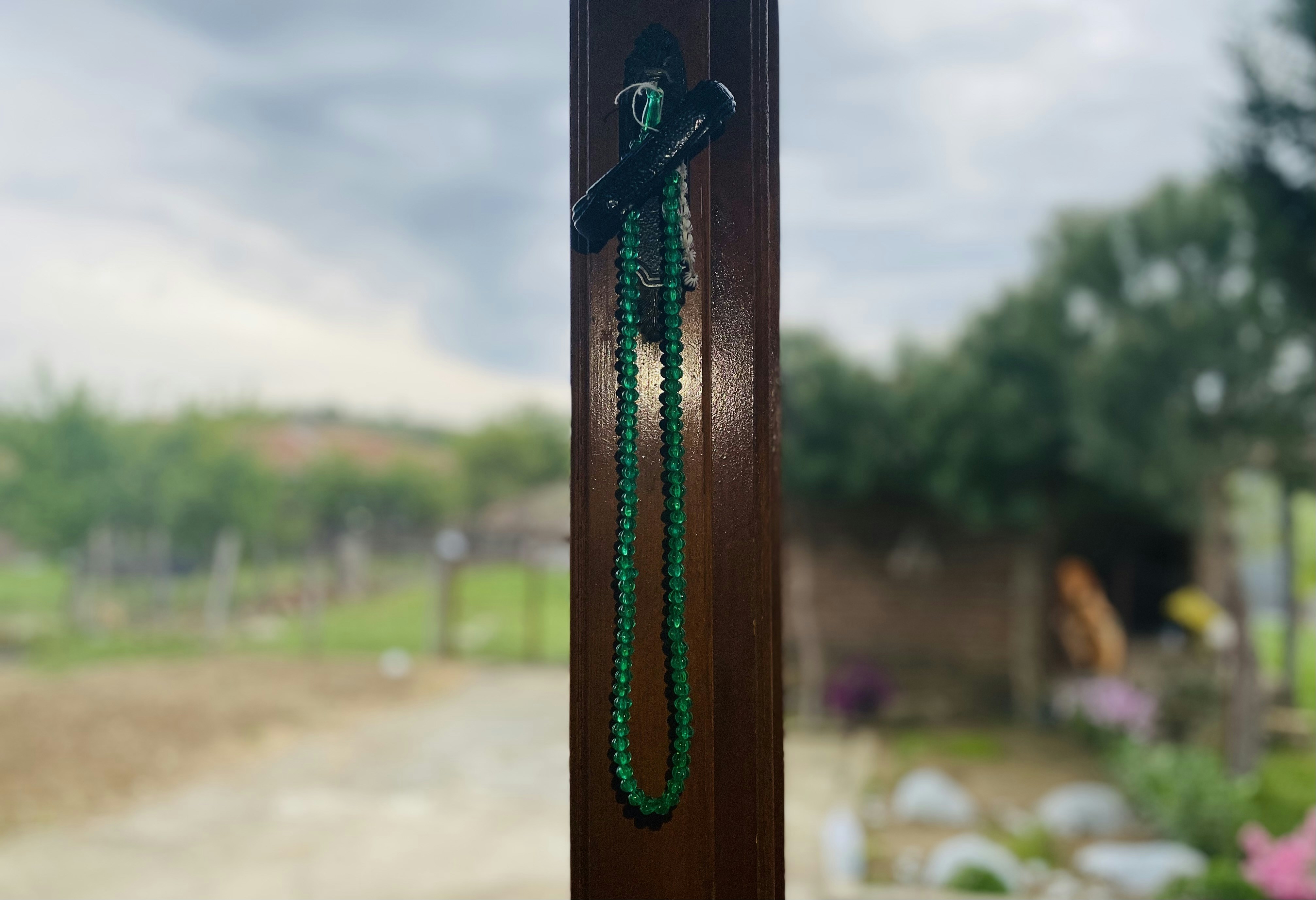 Dark stone prayer beads on aged wooden surface, deep shadows, candlelight, moody spiritual atmosphere