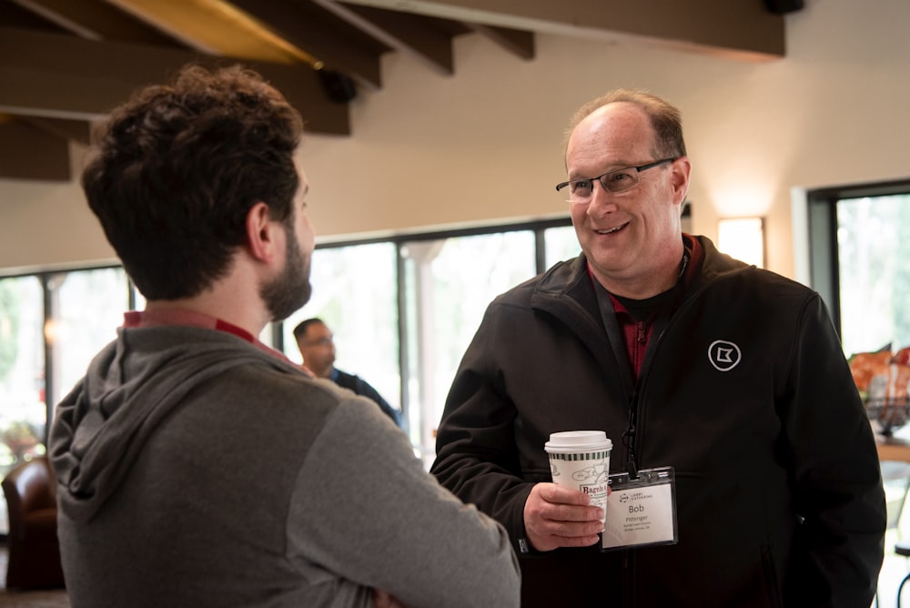 a man holding a cup and smiling at another man