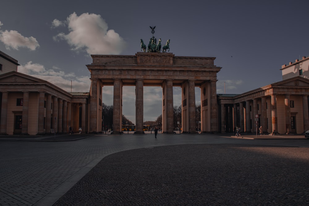 a large stone archway with statues on top with Brandenburg Gate in the background