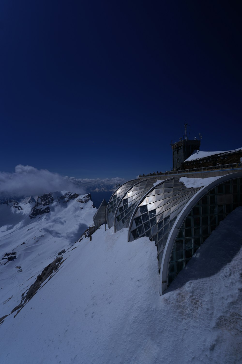 a building with a glass wall and a bridge over a snowy mountain