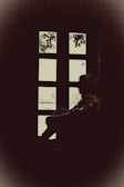 A silhouette of a person sitting alone by a window, lost in thought.