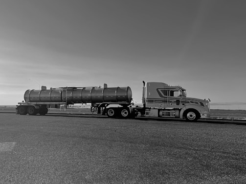 Photo of a fuel tanker truck parked at a loading bay under a clear blue sky.