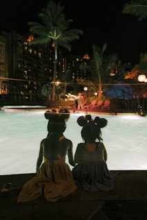 a group of women sitting on a bench by a pool at night