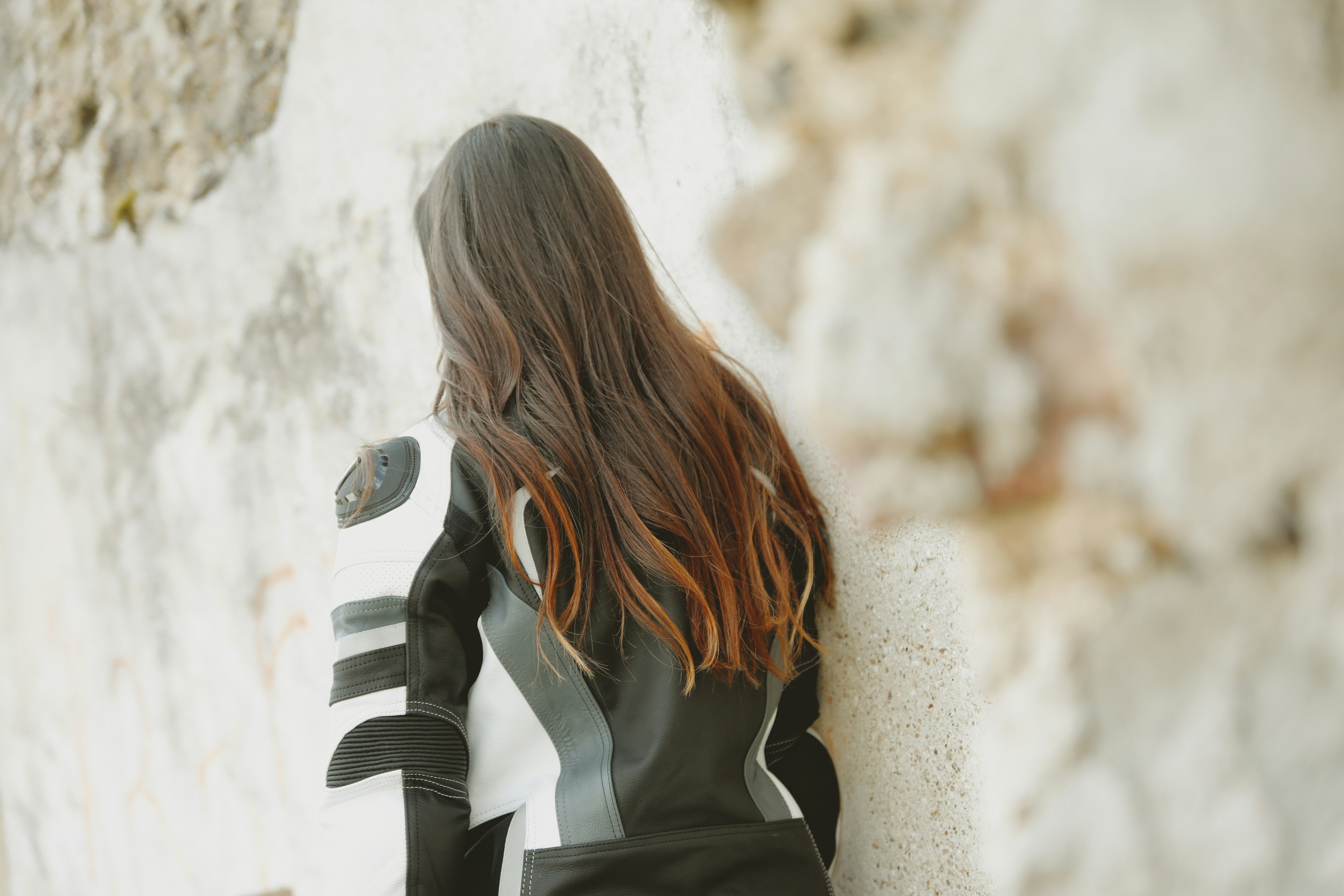 a woman wearing a black and white garment and holding a gun, Junge Frau in Lederkombi vor Natursteinwand // Young woman in a leather suit in front of a natural stone wall