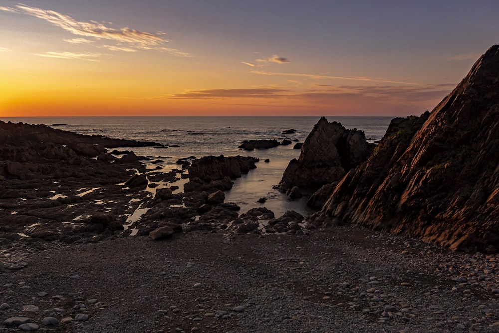 Una playa rocosa con una puesta de sol
