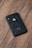 A black smartphone with an Apple logo is placed on a wooden surface, displaying its back panel. The phone's camera and flash are visible at the upper corner.