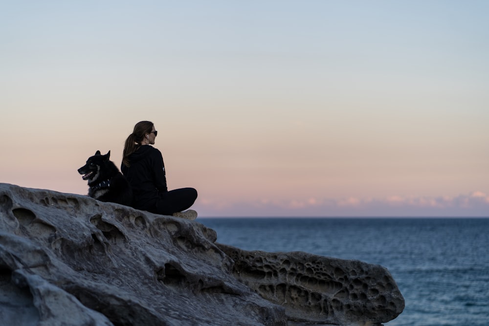 a man and a dog sitting on a rock by the water