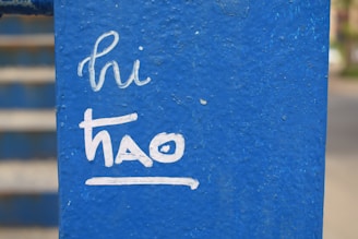 White handwritten text on a textured blue surface reads 'hi thao'. The background shows blurred steps or stripes in similar blue tones.