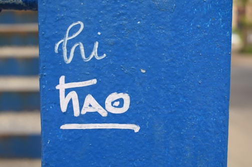 White handwritten text on a textured blue surface reads 'hi thao'. The background shows blurred steps or stripes in similar blue tones.
