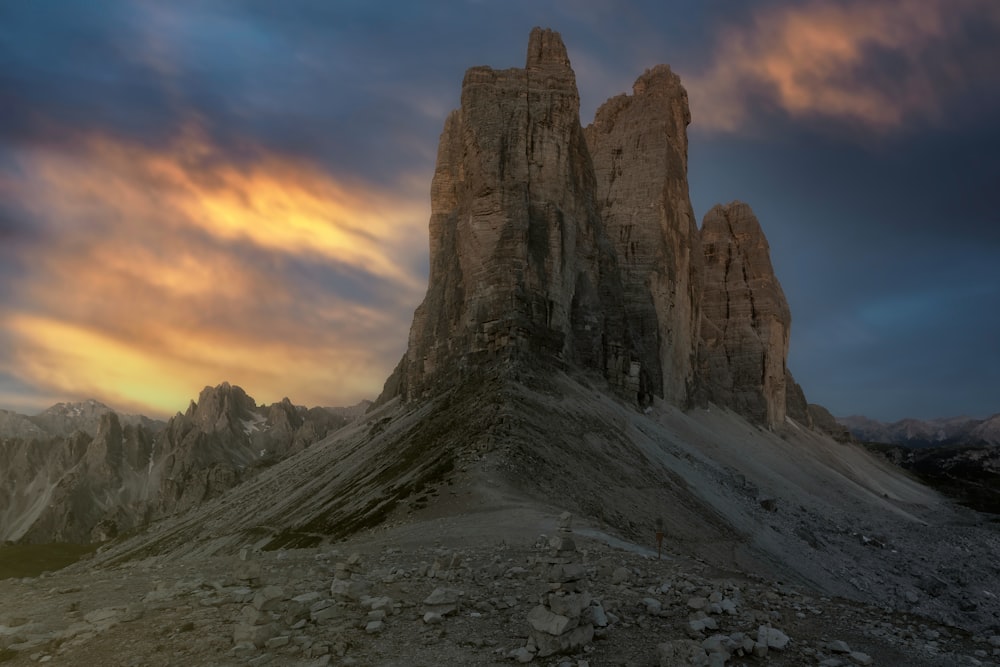 una montagna rocciosa con un tramonto con le Tre Cime di Lavaredo sullo sfondo