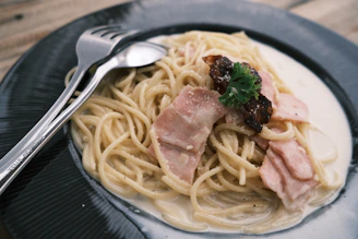 A steaming plate of spaghetti carbonara garnished with fresh parsley and parmesan.