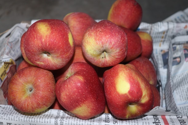 A pile of red apples with yellow patches arranged in a basket lined with newspapers, displaying a fresh and natural appearance.