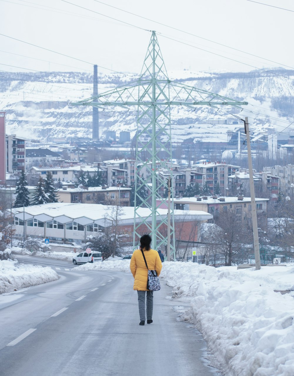 a man walking on a road with snow on the side and a large tower in the background