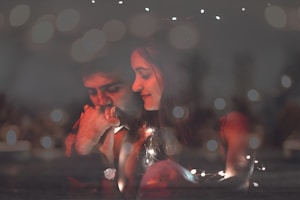 A tender and intimate moment is captured between a couple surrounded by a soft, dreamy bokeh effect. The man appears contemplative, resting his chin on his hand, while the woman looks at him with a gentle smile. Warm lighting creates a cozy and romantic atmosphere.