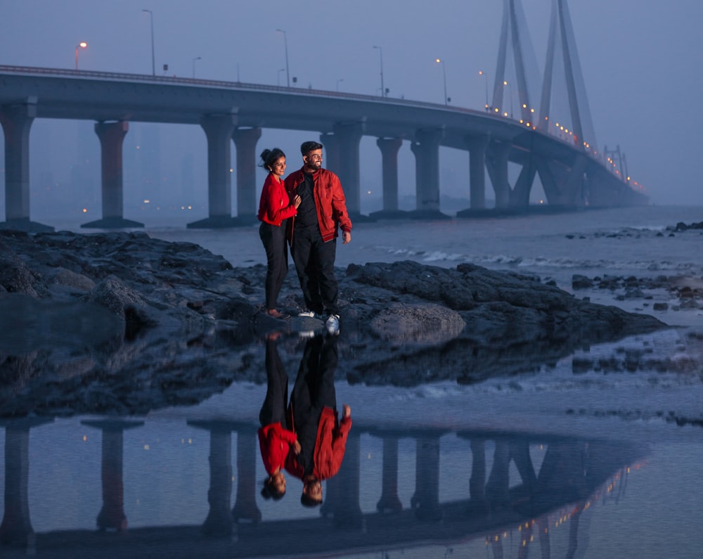 a couple of men standing on a rock in front of a bridge