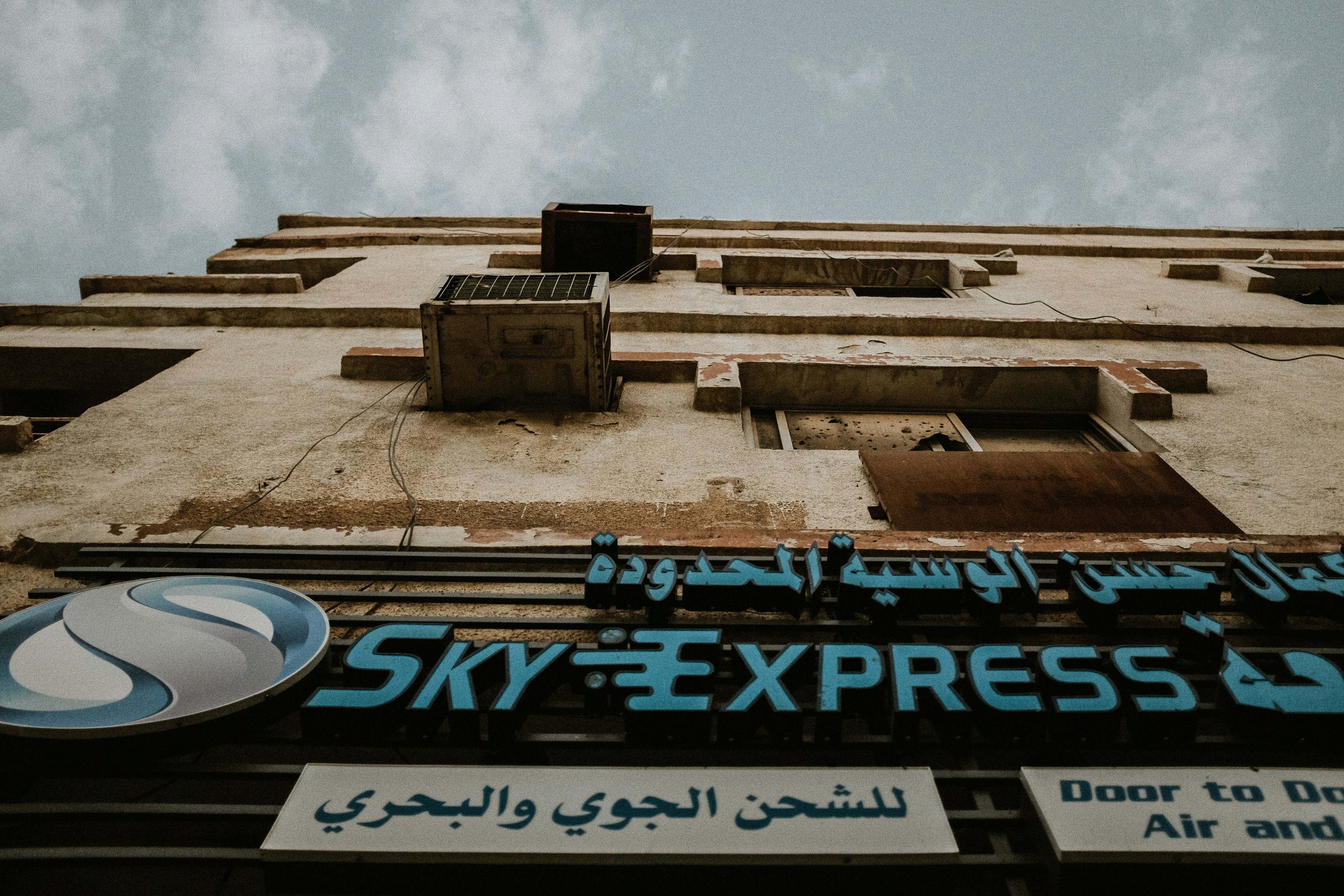 An image showing a chaotic airport departure board with multiple 'Cancelled' statuses, and distressed passengers. In the background, a faint map of the Middle East with tension points.