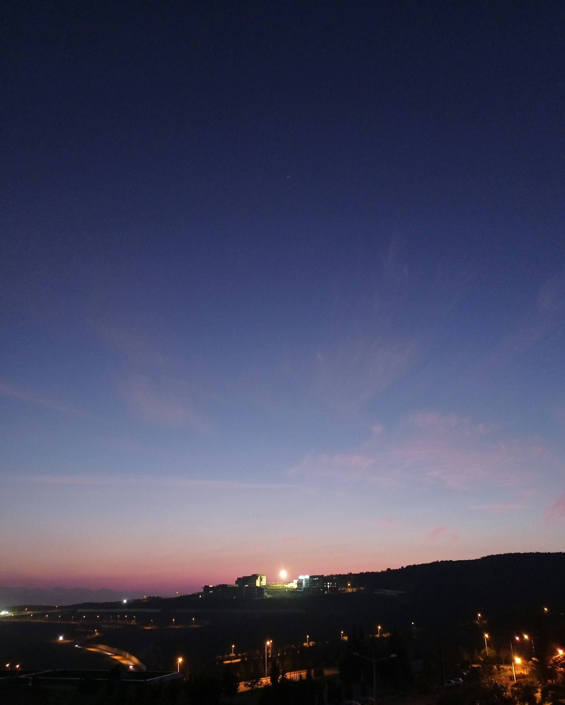 A stunning twilight view of The Satluj Vista's grand entrance, illuminated with warm golden lights against a deep navy sky.