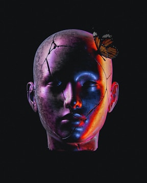 A sculpture-like human head with visible cracks and surreal, colorful lighting. A butterfly is perched gracefully on the head, offering a contrast between fragility and resilience.