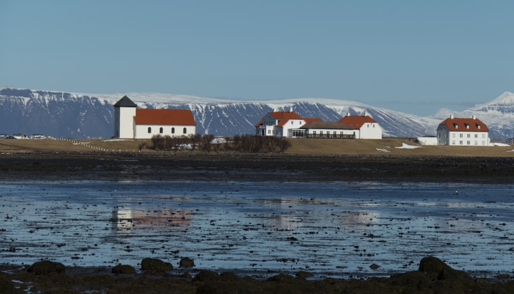 a group of buildings by a body of water with snow covered mountains in the background