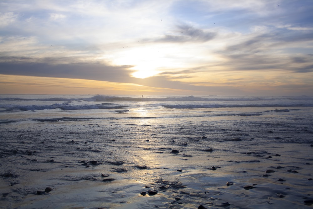 a beach with waves and the sun setting