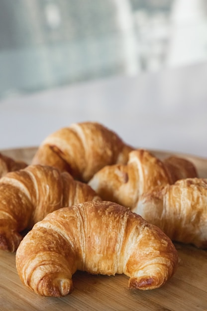 A close-up of golden, flaky croissants and savory tarts arranged on a rustic wooden table.