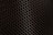 A close-up view of a metal mesh with a hexagonal pattern creating a honeycomb-like structure. The mesh is in a dark color against a black background, showcasing its intricate geometric design.