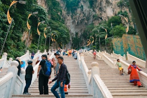 a group of people walking up stairs with Batu Caves in the background
