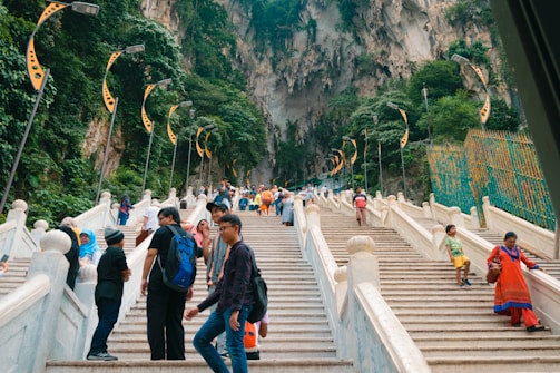 a group of people walking up stairs with Batu Caves in the background