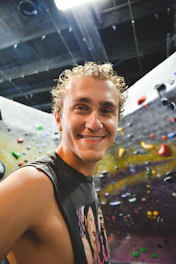 A smiling instructor guiding a beginner climber on a colorful indoor climbing wall.