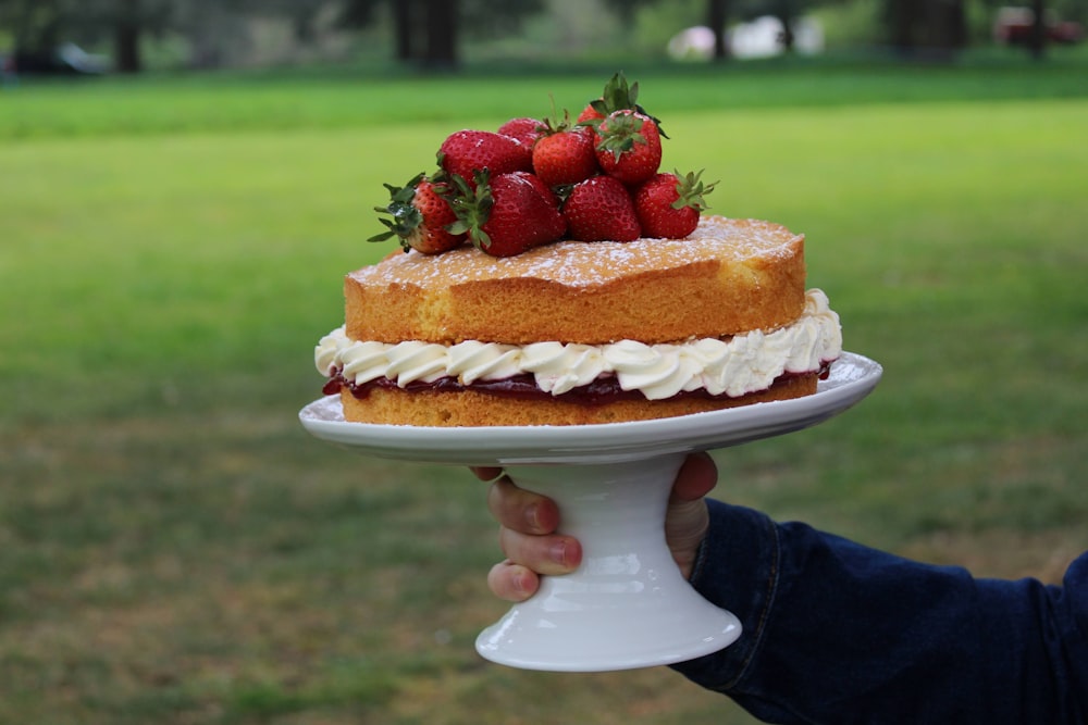 a person holding a cake with strawberries on top