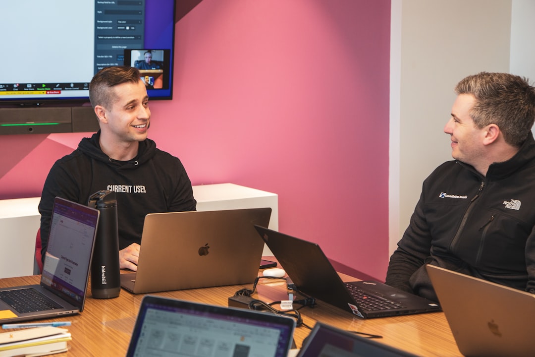 a couple of men sitting at a table with laptops, Smiling developers working together happily.