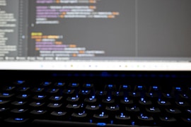 Close-up of hands coding on a keyboard with blue-electric highlights on the screen.