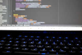 A close-up of hands typing on a keyboard with code on the screen.