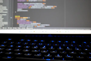 Close-up of hands typing code on a laptop with futuristic blue lighting in the background.