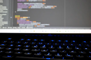 Close-up of hands typing on a keyboard with code on the screen, symbolizing custom software development.