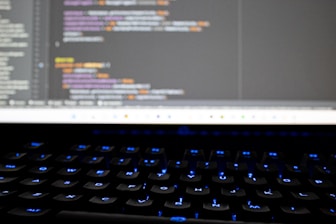 A close-up of hands typing on a keyboard with code on the screen.