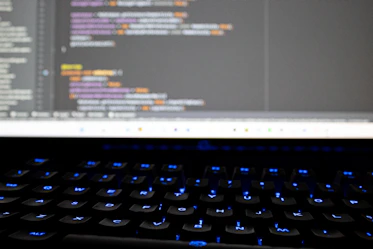 Close-up of hands typing code on a computer keyboard with colorful screen reflections.