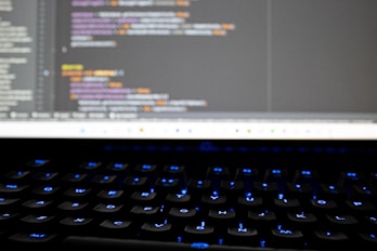 Close-up of hands typing on a sleek keyboard with code and cloud icons floating above.