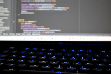 Close-up of hands typing on a keyboard with AI-generated code glowing on the monitor.